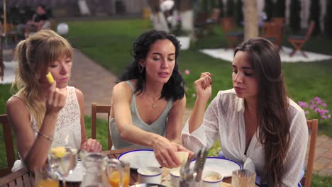 Tres-Mujeres-Alegres-Descansando-Hablando-Bebiendo,-Comiendo-En-Verano-Veranda-Café-Casual-Ciudad-Amistad-Modelos-Al-Aire-Libre