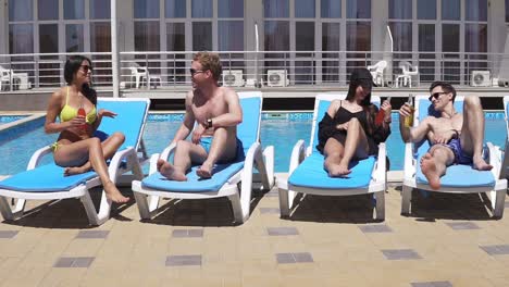 Happy-Young-People-Lying-On-Sunbeds-By-The-Swimming-Pool-And-Having-Fun