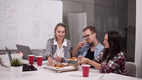 Grupo-De-Compañeros-De-Trabajo-Masculinos-Y-Femeninos-Almorzando-Comiendo-Pizza-Juntos-En-La-Oficina,-Jóvenes-Miembros-Del-Personal-Vestidos-Informalmente-Recreando-Después-De-Terminar-Las-Tareas