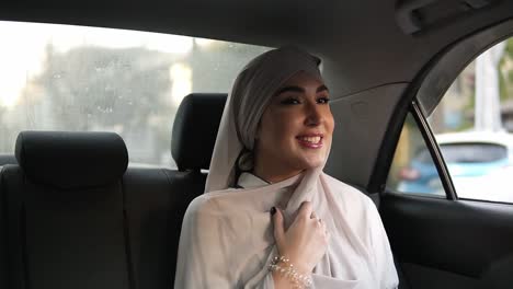 Porträt-Einer-Jungen-Muslimischen-Frau-Mit-Beigem-Kopftuch,-Die-Im-Auto-Sitzt,-Während-Sie-Aus-Dem-Fenster-Schaut,-Dann-Lächelt-Und-Für-Die-Kamera-Posiert