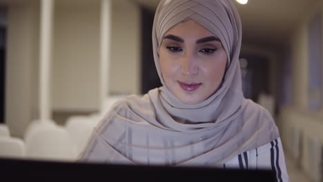 Nahaufnahme-Muslimisches-Weibliches-Gesicht-Mit-Beigem-Hijab,-Das-Online-Mit-Einem-Laptop-Im-Modernen-Konferenzsaal-Sitzt