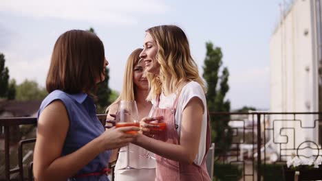 Three-Modern,-Young-Women-Are-Talking-And-Drinking-Orange-Cocktails-From-Wine-Glasses