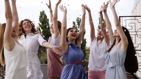 Group-Of-Young-Girls-Dressed-In-Casual-Partying-Outdoors-On-Terrace-Silver-Confetti-In-The-Air-At-Daytime-During-Their-Carefree-Hen-Party