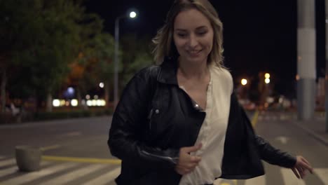 Young-Blonde-Woman-In-Jeans-And-Black-Leather-Jacket-Jumping-On-Yellow-Street-Bumpers-At-Night,-Having-Fun