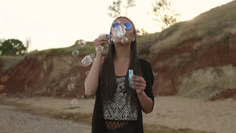 Young-Female-Hipster-With-Dreads-Cheerfully-Making-Soap-Bubbles-On-The-Beach-In-The-Evening