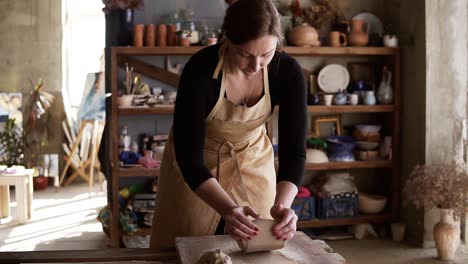 Front-View-Of-Female-Potter-Wearing-Beige-Apron-Kneading-Softly-Clay-Piece-On-Worktop,-Working-With-Her-Hands