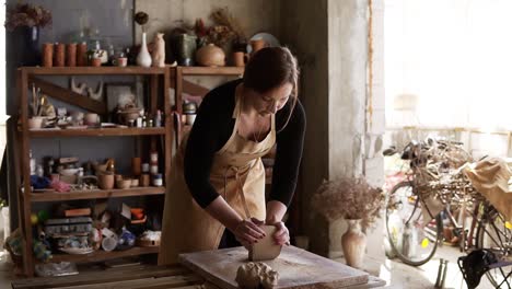 Front-View-Of-Female-Potter-Wearing-Beige-Apron-Kneading-Softly-Clay-Piece-On-Worktop,-Working-With-Her-Hands-1