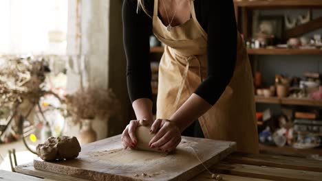 Front-View-Of-Female-Potter-Wearing-Beige-Apron-Kneading-Softly-Clay-Piece-On-Worktop,-Working-With-Her-Hands-2