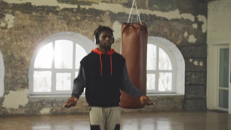 Male-Boxer-Skipping-The-Rope-In-An-Empty-Hall,-Listen-Music-In-Headphones