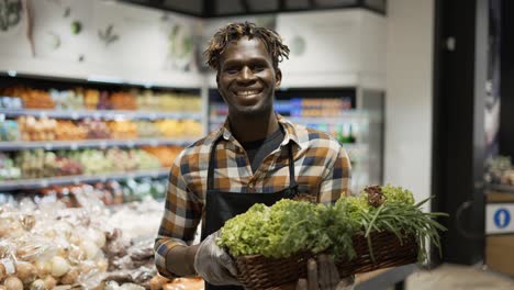 Portrait-Smiling-Worker-At-The-Store-With-Basket-Full-Of-Greens