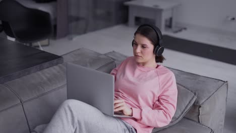 Frau,-Die-Mit-Laptop-computer-Arbeitet-Und-Musik-über-Kopfhörer-Auf-Einer-Couch-Hört