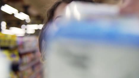 Close-Up-Portrait-Of-A-Young-Curly-Haired-Woman-Doing-Grocery-Shopping-At-The-Supermarket,-She-Is-Reading-A-Product-Label-And-Nutrition-Facts-On-A-Box