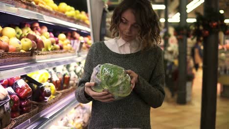 Mujer-Joven-En-Un-Supermercado-Moderno-Eligiendo-Repollo-Grande-En-El-Departamento-De-Verduras-Orgánicas-Y-Poniéndolo-En-Un-Carro