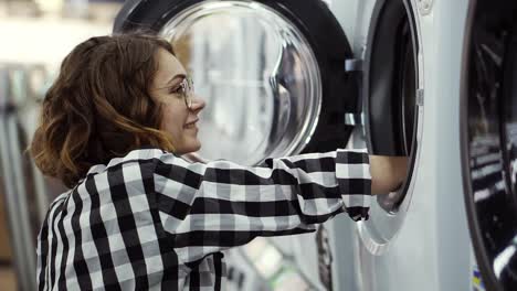 Eine-Junge-Positive-Frau-In-Einem-Karierten-Hemd,-Die-Sich-Im-Geschäft-Für-Haushaltsgeräte-Für-Eine-Waschmaschine-Entscheidet