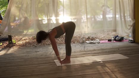 Young-Woman-Is-Doing-Yoga-In-Wooden-Hut-Filled-With-Light,-The-Girl-Performs-Yoga-Stands-And-Elements