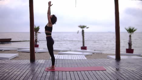 Junge-Frau-Macht-Yoga-Auf-Holzboden-Am-Strand,-Das-Mädchen-Führt-Yoga-stände-Und--elemente-Durch