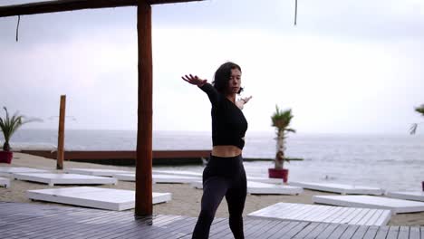 Mujer-Concentrada-Está-Haciendo-Yoga-En-La-Alfombra-En-La-Playa,-La-Niña-Realiza-Puestos-De-Yoga-Y-Elementos-Guerreros