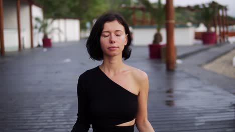 Woman-In-Black-Sitting-In-Lotus-Pose-Meditating-And-Breathing-Alone-Outdoors