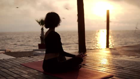 Yogi-Mädchen-Sitzt-Im-Sommer-Bei-Sonnenuntergang-In-Lotus-Pose-Vor-Dem-Meer-Und-Meditiert