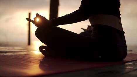 Silhouette-Of-Unrecognizable-Yogi-Girl-Sitting-In-Lotus-Pose-In-Front-The-Sea-Meditating,-Sunshining-Through-The-Hands-On-Knees