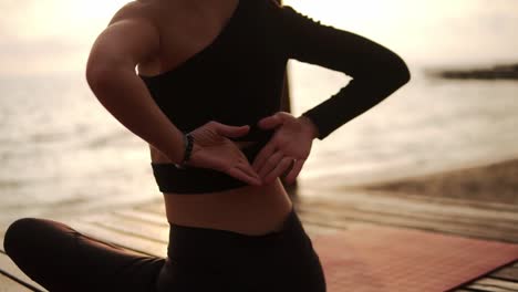 Mujer-Practicando-Yoga-Y-Estirando-La-Columna-Vertebral-Y-Las-Manos-Sentadas-En-La-Alfombra-En-El-Muelle-Del-Mar-Se-Une-A-Las-Manos-Detrás-De-Su-Espalda,-Vista-Rara