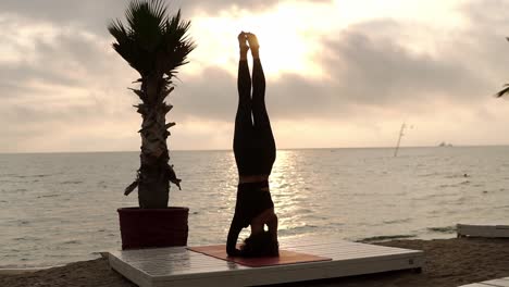 Woman-Standing-On-Head-In-Yoga-Pose-Salamba-Shirshasana-Outdoor,-Practicing-Yoga-Asana-On-The-Beach-In-Front-The-Sea
