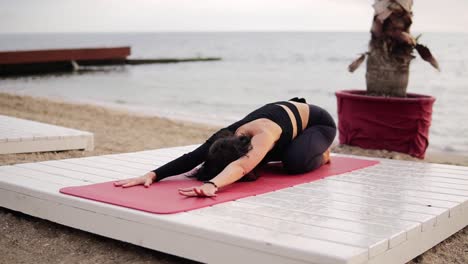 Frau,-Die-Yoga-Praktiziert-Und-Die-Wirbelsäule-Dehnt,-Die-Morgens-Auf-Der-Matte-Vor-Dem-Meer-Liegt