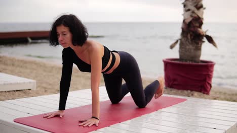 Mujer-Joven-Practicando-Yoga-Y-Estirando-La-Columna-Sobre-Una-Alfombra-Frente-Al-Mar-Por-La-Mañana