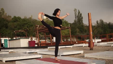 Frau,-Die-Yoga-Auf-Der-Matte-Am-Strand-Praktiziert,-Yoga-Asanas-Durchführt-Oder-Beine-Streckt,-Oberkörper-Mit-Angehobenem-Bein-Nach-Vorne-Lehnt