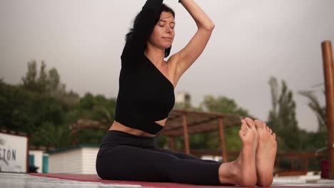 Schöne-Frau,-Die-Yoga-Auf-Der-Matte-Am-Strand-Praktiziert,-Yoga-Durchführt-Oder-Die-Beine-Dehnt,-Den-Oberkörper-Nach-Vorne-Lehnt