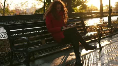 Young-Lady-Is-Reading-A-Book,-Red-Head-Lovely-Girl-Is-Sitting-On-Park-Bench,-Autumn-Colourful-Scene,-Lens-Flares,-Relax-In-City-Park