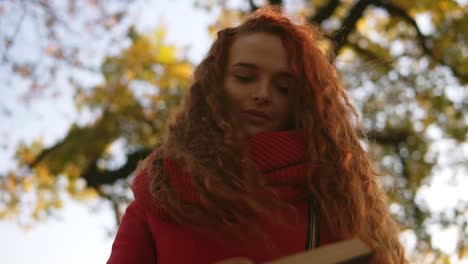 Portrait-Of-Pleased-Young-Lady-With-Long-Curly-Red-Hair-Sitting-On-Bench-And-Reading-Book-In-Park