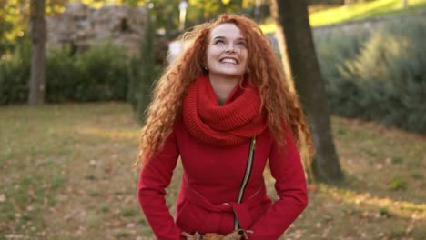 Portrait-Of-A-Happy-Red-Head-Woman-Throwing-Leaves-Around-And-Looking-Up-On-An-Autumns-Day