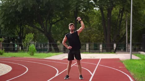 Full-Length-Of-A-Man-In-Black-Sportswear-Trains-With-Weight-Bob-Outdoors-Close-To-The-Stadium-On-The-Racetrack