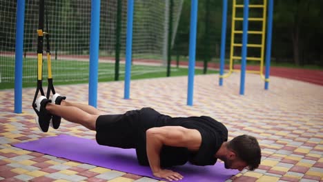 European-Man-Doing-Push-Ups-On-Mat-Using-Sport-Belts-Hanging-Legs-To-Strengthen-Exercise-Outdoors