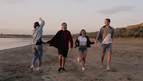 Full-Length-Shot-Of-Young-People-Running-Along-Seaside-With-Young-Girl-Turning-And-Trying-To-Run-Backwards
