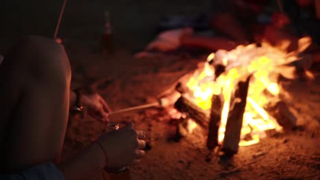 Close-Up-Of-A-Young-Hipster-Female-With-Headphones-On-Her-Neck-Frying-Marshmallow-On-Stick-From-Bonfire