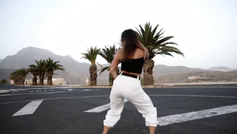 Girl-In-White-Is-Dancing-Outdoor-At-The-Road-With-Tropical-Trees-And-Hills-On-Background