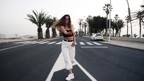 Excited-Young-Stylish-Woman-In-White-Pants-Posing,-Dancing-On-The-Road
