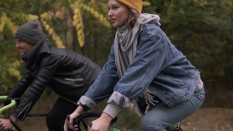 Happy,-Smiling-Friends-Or-Young-Couple-Cycling-Through-The-Autumn-Park-On-Bikes