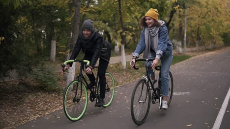Happy,-Smiling-Friends-Or-Young-Couple-Cycling-On-Their-Trekking-Bikes-Through-The-Autumn-Park-On-Bikes