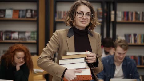 Slow-Motion-Footage-Of-A-Girl-In-Brown-Jacket-And-Glasses-Walking-By-Row-With-Pile-Of-Books-She-Took-From-The-Shelf