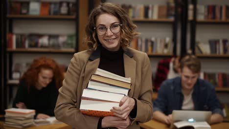 Porträt-Einer-Attraktiven-Europäischen-Studentin,-Die-Bücher-In-Der-Highschool-Bibliothek-Hält-Und-Lächelnd-In-Die-Kamera-Schaut