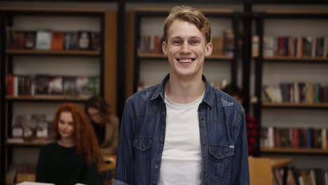 Close-Up-Portrait-Attractive-Young-Man-Laughing-Enjoying-Successful-Lifestyle-Achievement-Cheerful-Male-In-Library-Bookshelf-And-Classmates-On-Background-College-Education