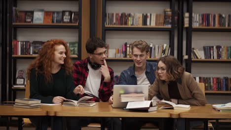 Group-Of-Young-Students-Talking-Using-Laptop-Explaining-Course-Work-Study-Together-In-Library-1