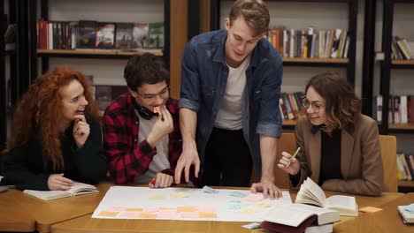 Group-Of-Young-Students-Of-Four-Explaining-Course-Work-Study-Together-In-Library