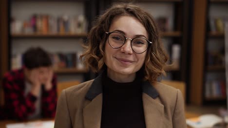 Porträt-Einer-Attraktiven-Kurzhaarigen-Europäischen-Studentin-Mit-Brille,-Die-In-Der-Bibliothek-Der-High-School-Steht-Und-Lächelnd-In-Die-Kamera-Schaut-Und-Lächelt