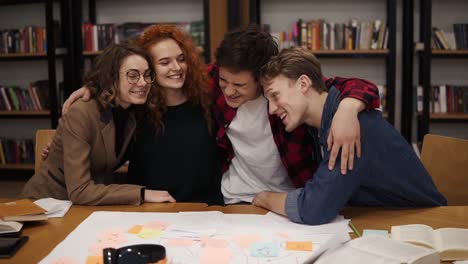 Portrait-Of-Diverse-Friends-Classmates-Sitting-At-The-Table-In-College-Library-Embracing,-Hugging-Each-Other