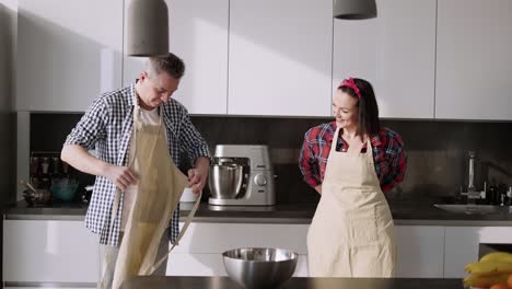 Cheerful-Couple-Cooking-Together-At-Home-In-The-Kitchen,-Putting-Aprons