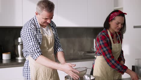 Portrait-Of-A-Couple-Sifting-Flour-To-Make-Bread-In-Kitchen-Together